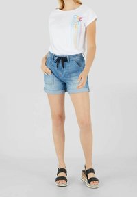 Valkoinen t-paita, jossa on "CREATE" -grafiikka, yhdistettynä vaaleansinisiin farkkushortseihin, joissa on kiristysnauha, käännetyt hihat ja sivutaskut. Mustat alustan sandaalit.