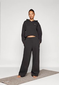 Čierna crop mikina s textúrovanou tkaninou a malým logom. Kombinovaná s voľnými čiernymi textúrovanými nohavicami. Model stojaci na svetlosivej podložke.