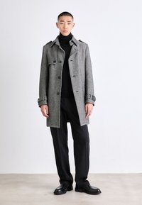 Grå yllemixrock med fiskbensmönster, stora slag, knäppt fram och justerbara manschetter. Kombinerad med svart polo och byxor.