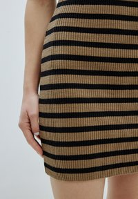 Abito a coste con strisce marroni e nere, design aderente, di lunghezza media, tessuto testurizzato, mano appoggiata sul fianco, che mette in mostra l'orlo.