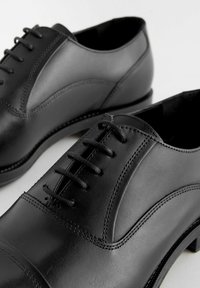 Black leather dress shoes with a smooth finish, featuring a lace-up design, round toe, and subtle stitching details along the sides.