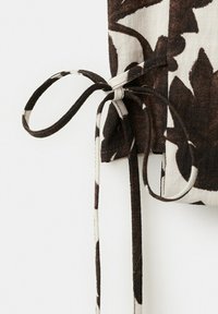 Tissu floral marron et blanc noué en un nœud avec deux extrémités pendantes sur un fond blanc uni.