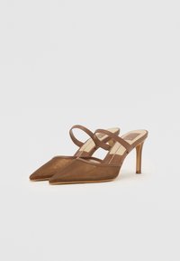 Talons hauts brun à bout pointu avec une tige en mesh transparent et deux fines brides. Design épuré avec un talon aiguille mince, texture lisse.