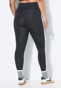 Leggings neri con vita alta, caratterizzati da strisce laterali bianche, texture liscia e design aderente. Indossati con calze a motivi e sneaker.