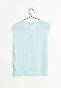 Top de manga corta azul claro hecho de tela suave y transparente, con un panel de satén vertical en la parte trasera, colgado de un gancho negro.