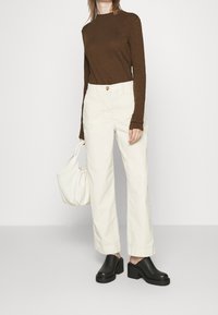 Bruine lange mouwen top, witte hoge taille broek, zwarte clogs en een witte schoudertas. Geweven stof en een ontspannen pasvorm.