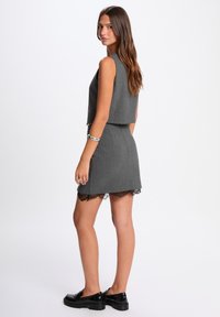 Completo grigio in due pezzi composto da un top senza maniche corto e una gonna aderente con orlo in pizzo. Texture liscia con righe verticali.