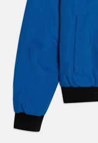 Niebieska kurtka typu bomber o gładkiej fakturze, z czarnymi, prążkowanymi mankietami oraz detalem bocznej kieszeni. Tkanina wydaje się lekka i trwała.