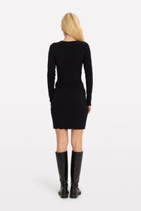 Abito lungo a maniche lunghe nero con un design aderente e orlo a scallop, abbinato a stivali in pelle nera al ginocchio.