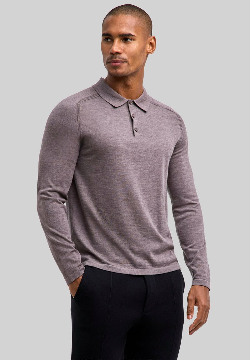 Koszulka polo z długim rękawem w jasnofioletowej tkaninie, z kołnierzykiem, trzema guzikami na patce oraz ściągaczami na mankietach. Gładka tekstura.