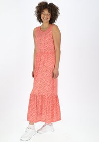 Maxikleid in Korallenfarbe mit Blumenmuster, ärmelloses Design und gestuftem Saum. Aus leichtem Stoff gefertigt, kombiniert mit weißen Sneakern.
