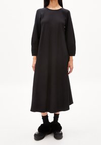 Zwarte lange mouwen jurk met een relaxte pasvorm, ronde halslijn, gladde stof en een vloeiende silhouet. Draag het met zwarte plateau schoenen en sokken.