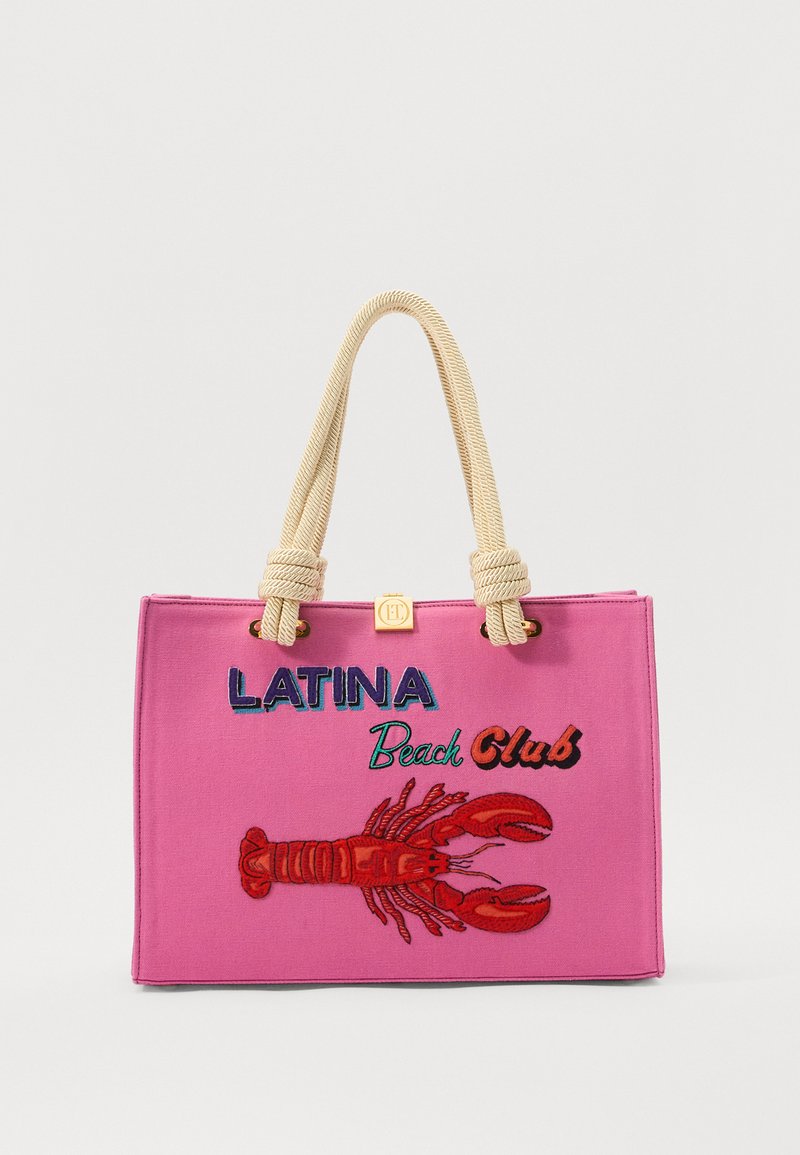 Geantă de podea roz din pânză cu mânere din frânghie; are un text brodat "LATINA Beach Club" și un design cu un homar roșu pe față.