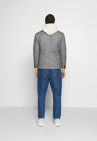 Graue Jacke aus Wollmischung mit hellfarbigem Kapuzen, kombiniert mit locker sitzenden Jeans und weißen Sneakern, von hinten gesehen.