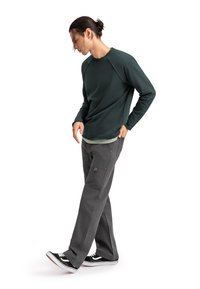 Felpa verde scuro con maniche lunghe, indossata sopra una maglietta verde chiaro. Pantaloni cargo grigi con tasche, abbinati a sneakers nere e bianche.