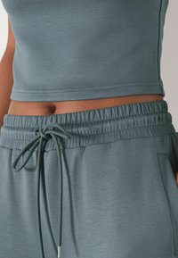Licht teal crop top met een gladde textuur en gestikte zoom, gecombineerd met bijpassende elastische broek met een trekkoord en zijzakken.
