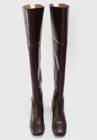 Hohe, dunkelbraune Lederstiefel mit seitlichen Reißverschlüssen und quadratischen Zehen, aufrecht stehend vor einem weißen Hintergrund.