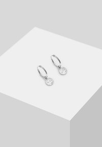Pendientes de aro de plata con un charm circular texturizado. El charm presenta una superficie clara y reflectante, lo que realza su atractivo decorativo.