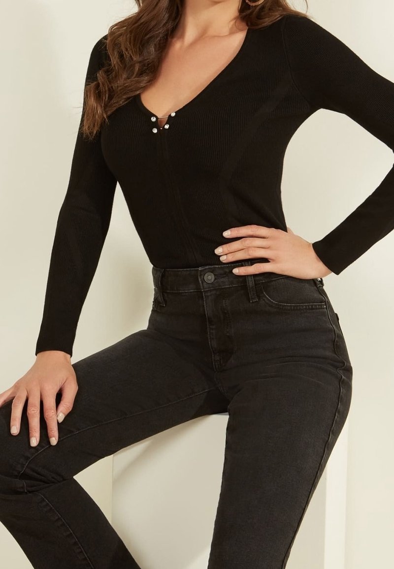 Schwarzer, gerippter Body mit V-Ausschnitt und dekorativen Knöpfen. Kombiniert mit hochtaillierten schwarzen Jeans, die eine klassische Denim-Textur und Passform aufweisen.