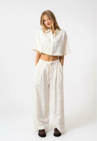 Camicia a bottoni corta di colore crema e pantaloni larghi realizzati in tessuto leggero. Presenta una vita con cordoncino e un sottile motivo testurizzato.