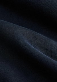 Tmavomodrá látka s hladkým povrchom, s diagonálnymi tkaninovými vzormi a jemným leskom. Zameranie na záhyby a odrazy svetla.