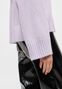 Πλεκτό πουλόβερ λεβάντας με ριμπ υφή και απαλό ύφασμα, συνδυασμένο με γυαλιστερό μαύρο παντελόνι. Το τελείωμα και οι μανσέτες έχουν διακριτό ριμπ σχέδιο.