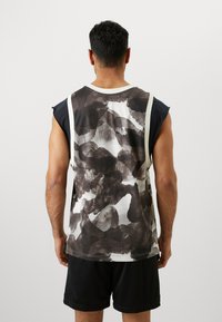 Camisa atlética sin mangas en blanco y negro con un patrón abstracto y texturizado. Presenta un escote blanco en contraste y acentos laterales.