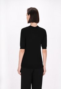 Top tricot negru cu mânecă scurtă și decolteu rotund, având o textură netedă și un design minimal, asortat cu pantaloni negri evazați.