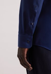 Navyblauwe, getextureerde langarmshirt met knoopmanchetten; heeft subtiele details op de manchetten en een nette zoom.