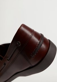 Chaussure en cuir marron avec une finition lisse, un bout arrondi et des détails de couture subtils. Semelle foncée avec une légère élévation au talon.