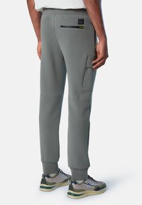 Hellgraue Jogginghose mit schmalem Schnitt, ausgestattet mit einer schrägen Cargo-Tasche und einer mit Reißverschluss versehenen Gesäßtasche. Elastischer Bund und Bündchen.