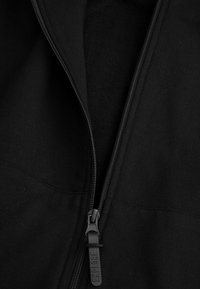 Czarna bluzka z zamkiem błyskawicznym, z teksturowanym wnętrzem. Posiada solidny zamek i gładki materiał, o prostym, funkcjonalnym designie.