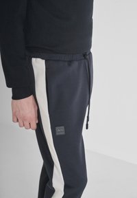 Navy sweats met crèmekleurige zijstrepen en een trekkoord in de taille, voorzien van een klein zwart merkje op de dij. Gemengd katoen materiaal.