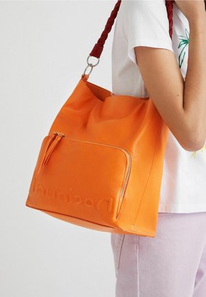 Sac fourre-tout en cuir orange avec une bandoulière tressée rouge. Comprend une poche zippée à l'avant et un logo embossé sur le côté. Texture lisse.