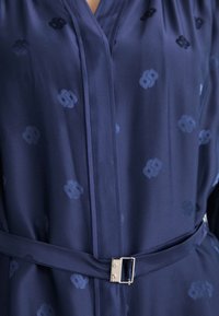 Abito avvolgente blu navy in satin con un motivo sottile, caratterizzato da una vita con cinta e dettagli in metallo argentato sulla fibbia della cintura.
