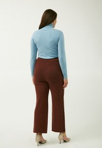 Hellblaues Rollkragenoberteil, tailliert, kombiniert mit braunen, weitgeschnittenen Strickhosen mit seitlichem Zopfdetail. Beigefarbene Absätze.
