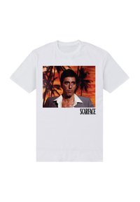 Bílý bavlněný tričko s grafikou muže na pozadí západu slunce s palmami a textem "SCARFACE" v černé barvě.