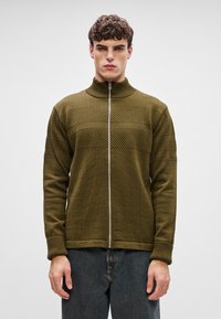 Knit zip-up jacket in dark olive green with textured horizontal stripes and ribbed cuffs. Lightweight fabric, fitted design, and stand collar.