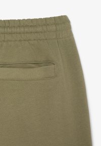 Pantalones deportivos verde oliva con una textura suave y lisa, que cuentan con una cinturilla ancha y un pequeño bolsillo trasero con una abertura horizontal.