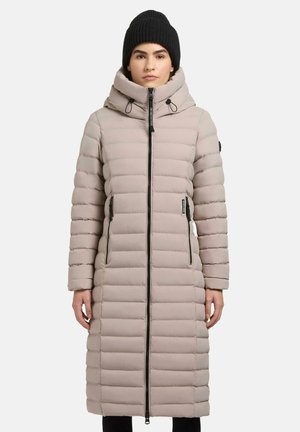 Lichtbeige pufferjas met verticale quiltstructuur, lange lengte, hoge kraag, ritssluiting aan de voorkant en zijzakken. Draagt een zwarte gebreide beanie.