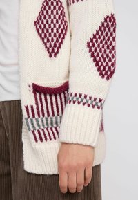 Cardigan a maglia in crema con motivo a rombi bordeaux e strisce. Presenta una tasca frontale e polsini a coste, evidenziando un tessuto testurizzato.