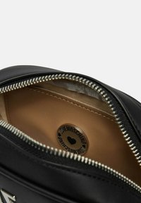 Interno di una borsa in pelle nera con una fodera color cammello, zip argentata e un'etichetta rotonda con un cuore e il nome del marchio. Texture liscia.