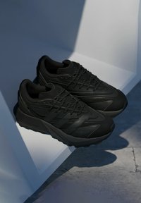 Czarne buty sportowe z teksturowaną cholewką, panelami z siateczki i zakrzywioną podeszwą. Posiadają zapięcie na sznurowadła i subtelne logo po boku.