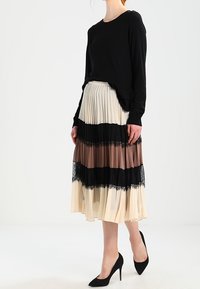 Svart långärmad tröja i kombination med en plisserad kjol med horisontella ränder i svart, brunt och beige med spetsdetaljer. Svarta klackar.