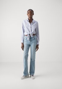 Blå og hvit stripete skjorte med knute i livet, kombinert med lyseblå utvidede jeans og grå joggesko. Enkel design, avslappet utseende.