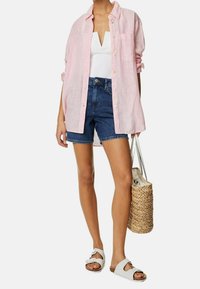 Lichtroze gestreepte shirt, witte top, donkerblauwe denimshorts en beige sandalen. Een bruine gehaakte tas maakt de look compleet.