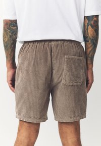 Braune Cord-Shorts mit vertikaler Rippung, elastischem Bund und einer Gesäßtasche. Das Material wirkt weich und hat eine strukturierte Oberfläche.