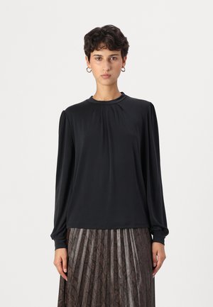 Black long-sleeve blouse with a round neckline and pleated detailing at the shoulders, paired with a pleated dark patterned skirt.