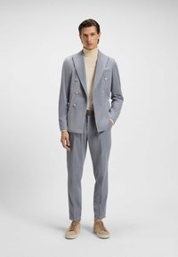 Blazer doppiopetto azzurro chiaro in tessuto texturizzato, abbinato a pantaloni coordinati e un dolcevita beige. Sneakers in una tonalità neutra.