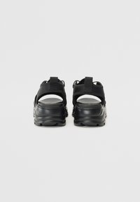 Black sandals with textured straps and a cushioned sole, featuring a sporty design and adjustable heel loop for secure fitting.
